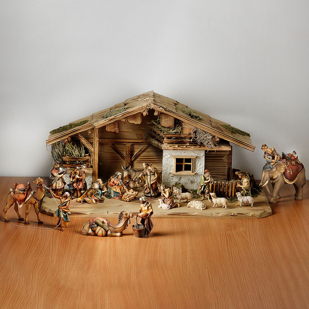 Handgeschnitzte Krippe aus Holz mit 20 detailreichen Figuren, darunter die Heilige Familie, die Heiligen Drei Könige, Hirten, verschiedene Tiere und ein Stall. Die Szene ist traditionell gestaltet und eignet sich als festliche Weihnachtsdekoration auf einer Holzoberfläche.