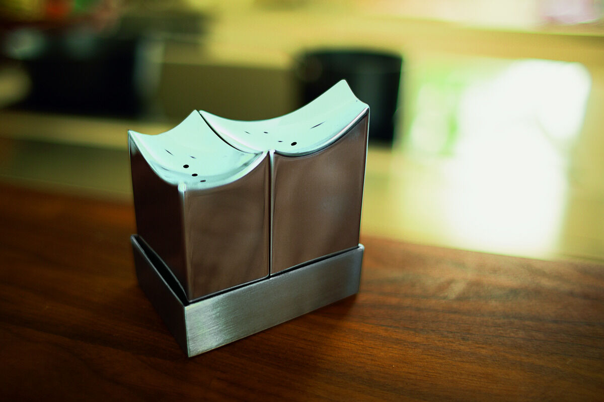 Salz- und Pfefferstreuer in moderner Form, inspiriert von der Architektur der Elbphilharmonie. Hergestellt aus Edelstahl, stehend auf einem Holztisch in einem Küchenumfeld.