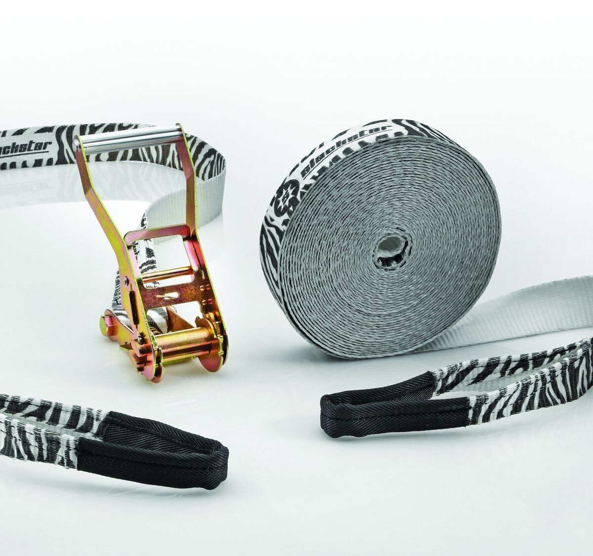 Ein Slackline-Set mit Zebra-Muster, bestehend aus einem langen, weißen Gurtband mit schwarzen Streifen, einer goldenen Ratsche und schwarzem Schutzmaterial.