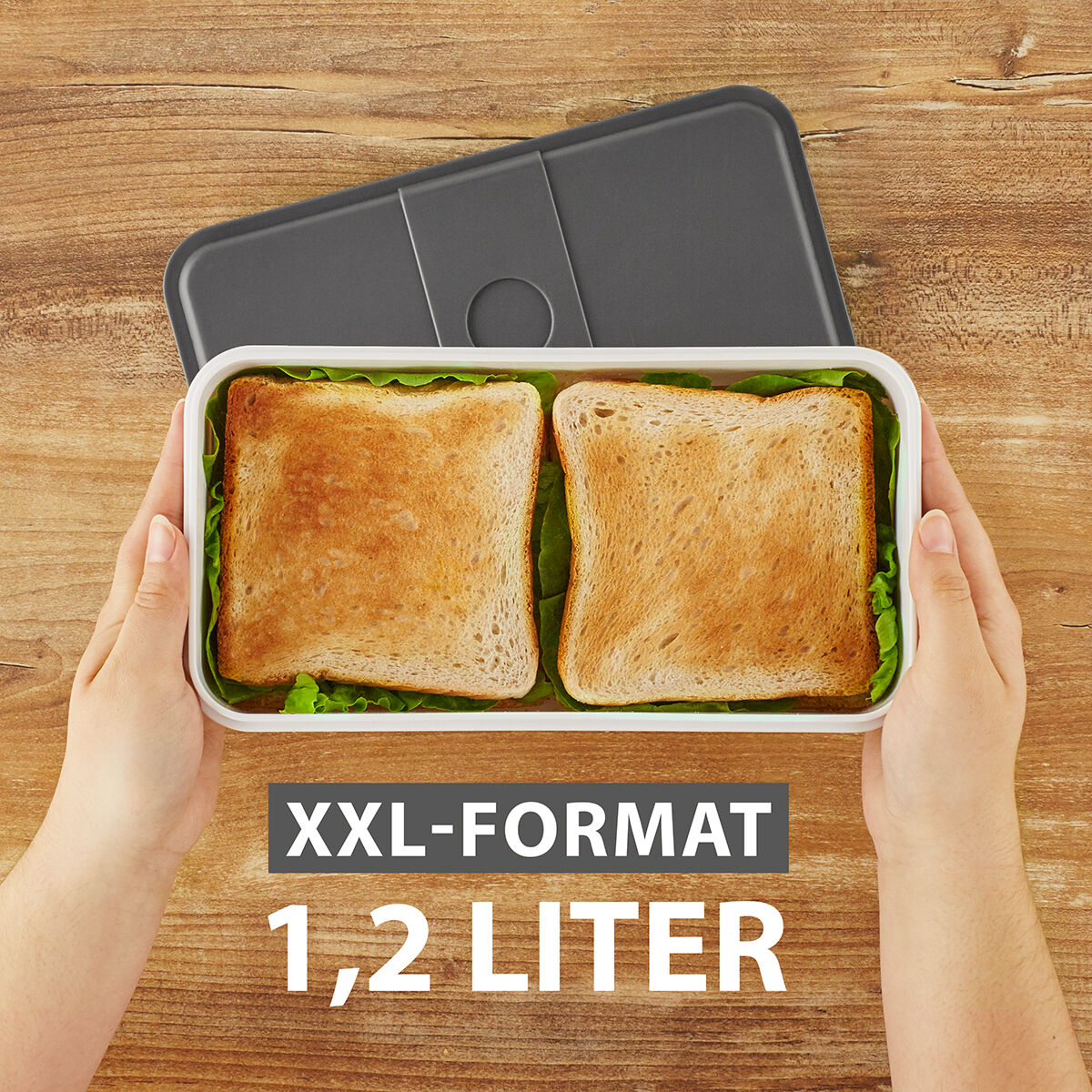 Eine XXL-Lunchbox mit einem Fassungsvermögen von 1,2 Litern, gefüllt mit zwei Brotscheiben, gehalten von zwei Händen auf einem Holztisch.