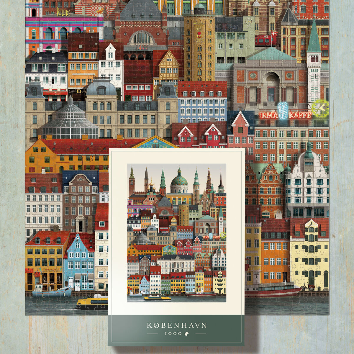 Das Bild zeigt ein fast fertiggestelltes 1000 Teile Puzzle mit einer detailreichen und farbenfrohen Illustration der Stadtansicht von Kopenhagen, darunter das Puzzlemotiv auf dem Karton. Im Vordergrund sind zahlreiche Häuser, Türme und markante Gebäudedächer zu sehen. Die Puzzlefläche liegt auf einem hellblauen Holztisch und oben rechts sind einige lose Puzzleteile sichtbar.
