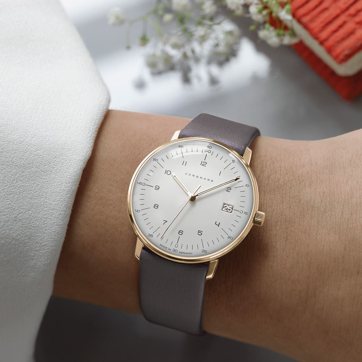Junghans Armbanduhr für Damen aus der ZEIT-Sonderedition »max bill Damen«, mit einem schlichten weißen Zifferblatt, goldenen Zeigern und Gehäuse, braunem Lederarmband, und einem Kalenderfenster bei 3 Uhr.