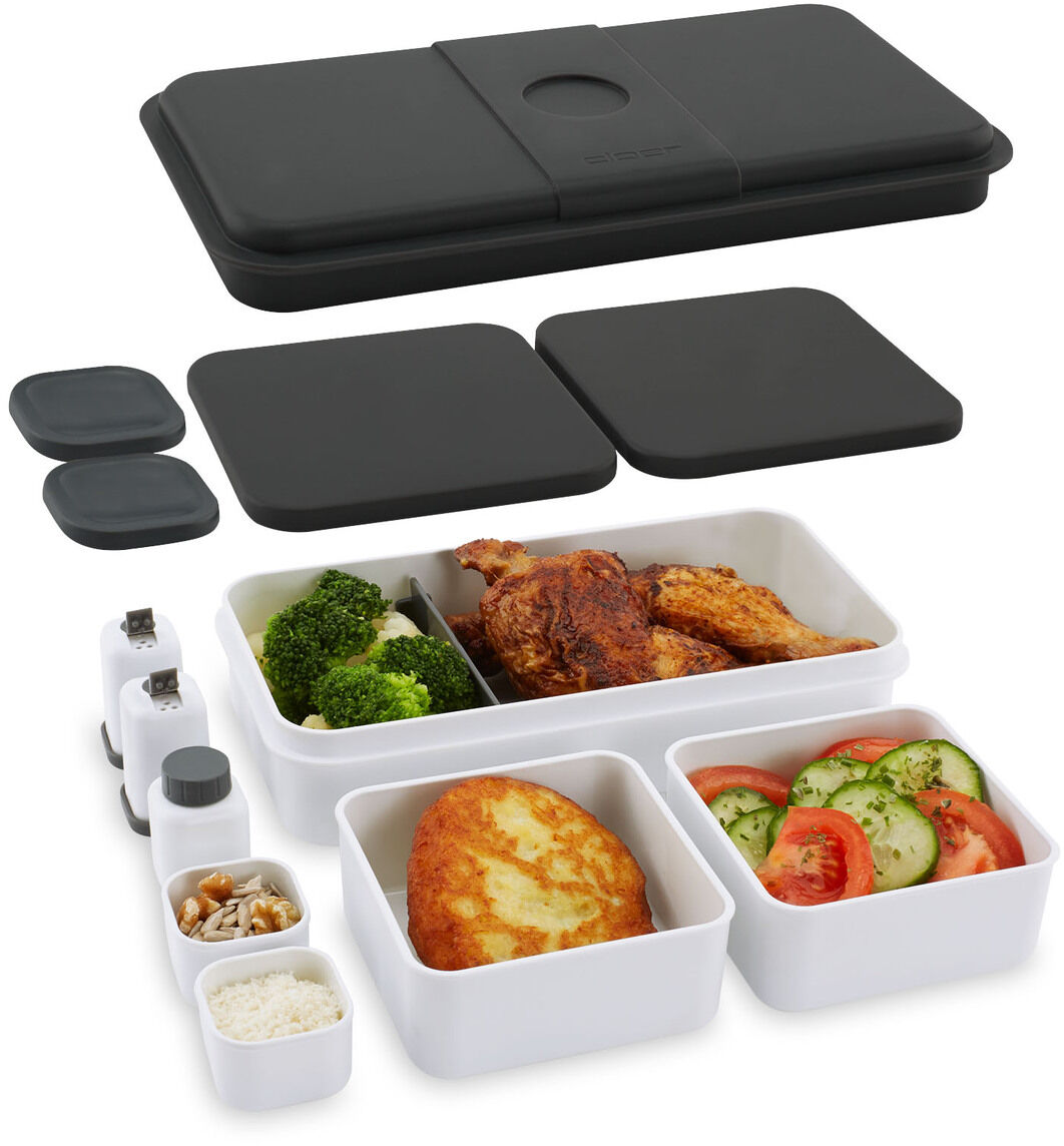 Ein Lunch Care System mit mehreren Fächern für verschiedene Arten von Lebensmitteln, einschließlich Gemüse, Fleisch, und Beilagen. Die Essensbehälter sind schwarz und weiß und bestehen aus abnehmbarem Deckel und verschiedenen kleineren Behältern.