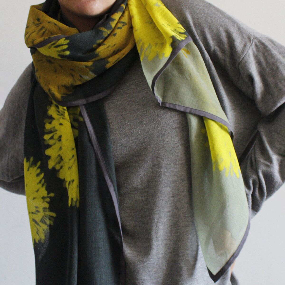 Wollschal »Carol« in Gelb und Grau mit abstraktem Muster, um den Hals einer Person gelegt und über einem schlichten grauen Pullover getragen, modisches Accessoire für kühle Tage.