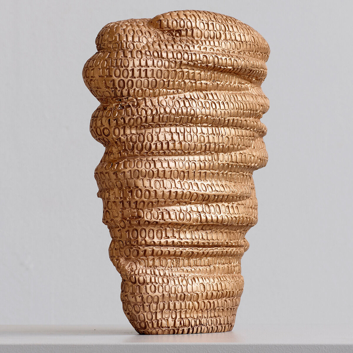 Eine goldene Skulptur mit auffälliger Binärcode-Textur, die sich in geschwungenen, wellenartigen Formen nach oben bewegt.