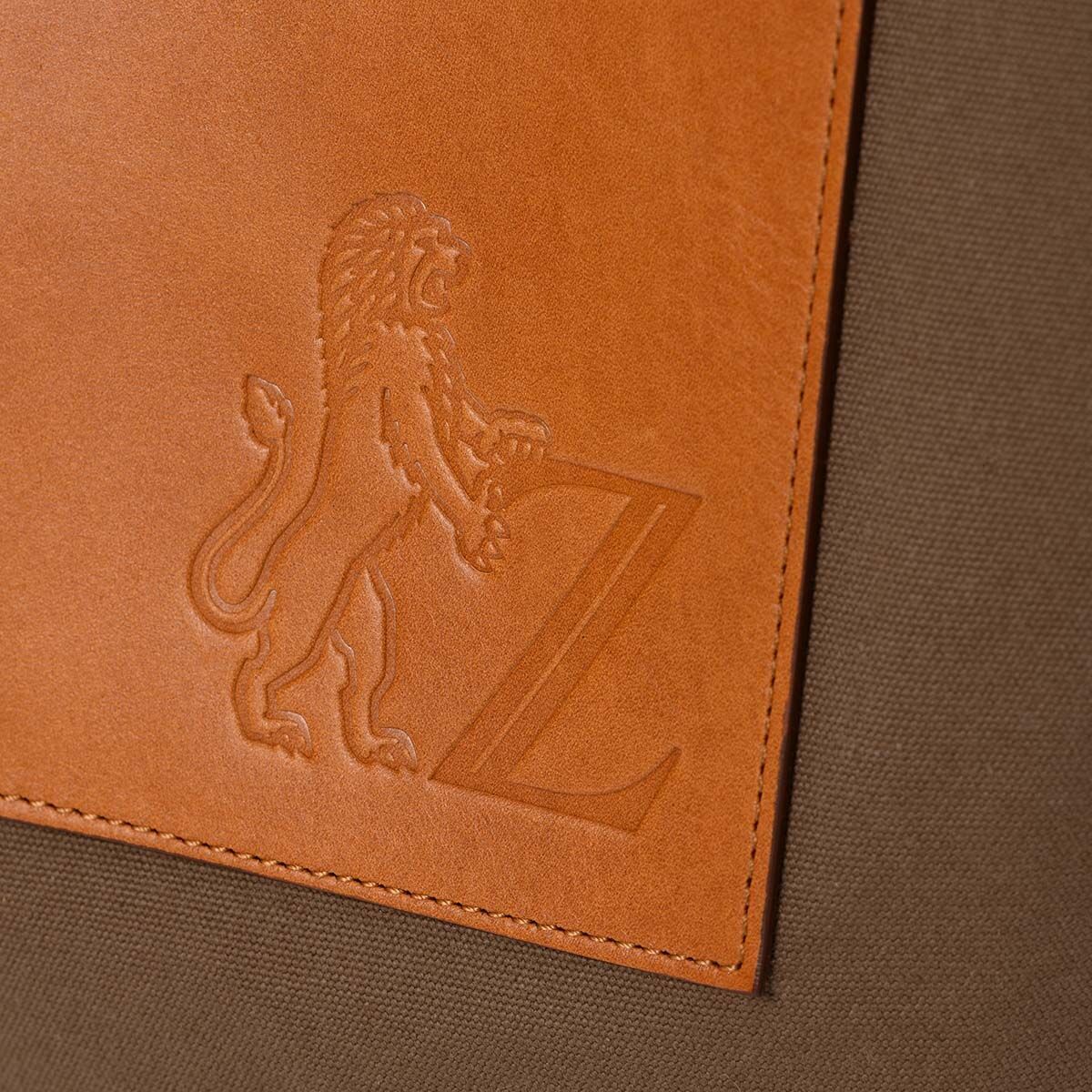 Detailansicht einer Jubiläums-Markttasche aus braunem Leder mit einem geprägten Löwendesign und einem Buchstaben Z, auf einem beige Hintergrund.
