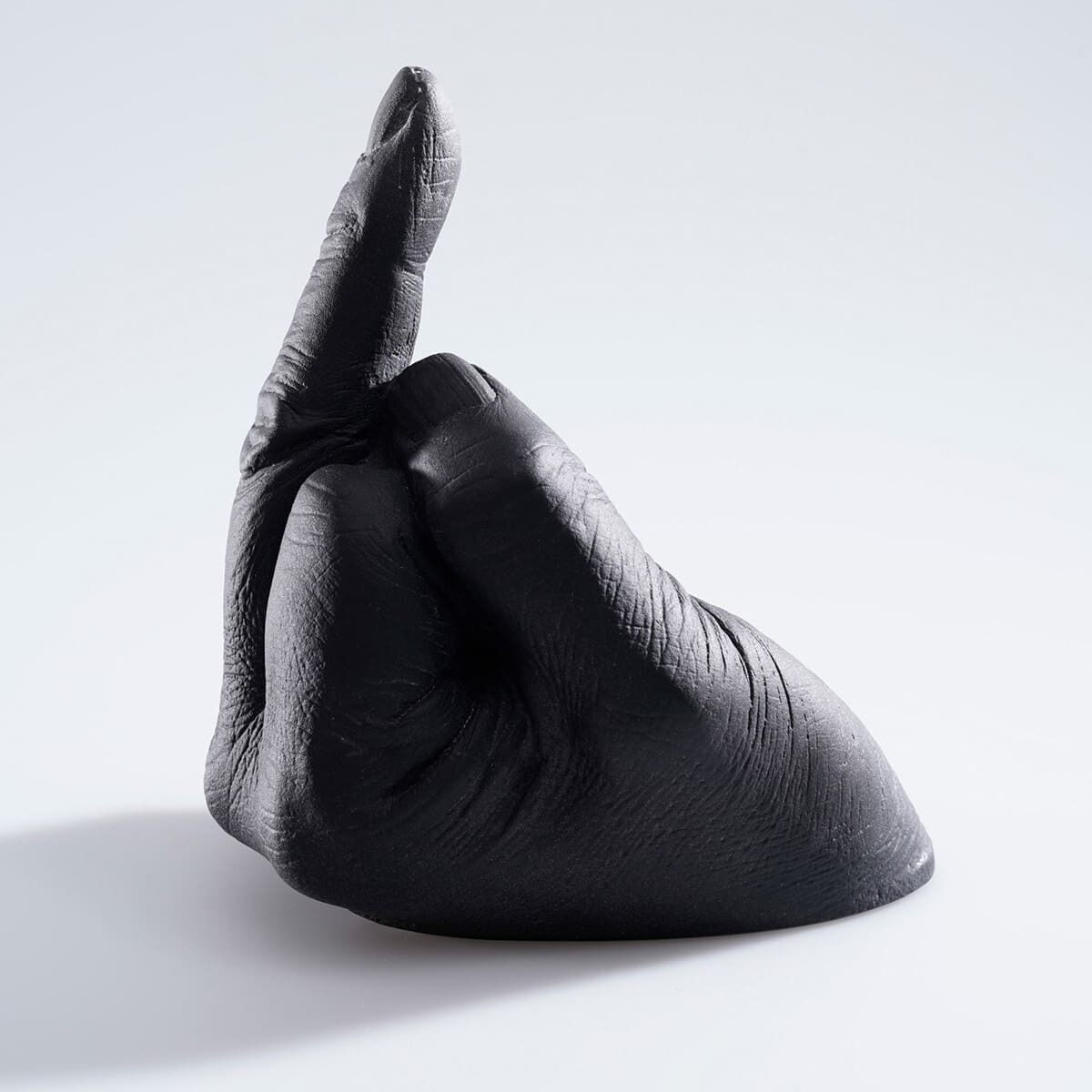 Diese Skulptur ist eine kunstvolle Darstellung einer Hand, die in einer protestähnlichen Geste zeigt. Es handelt sich um eine Arbeit von Ai Weiwei aus Glas mit einer dunkelgrauen bis schwarzen Farbgebung. Die Skulptur hat eine strukturierte Oberfläche und ist auf einem hellen Hintergrund platziert.