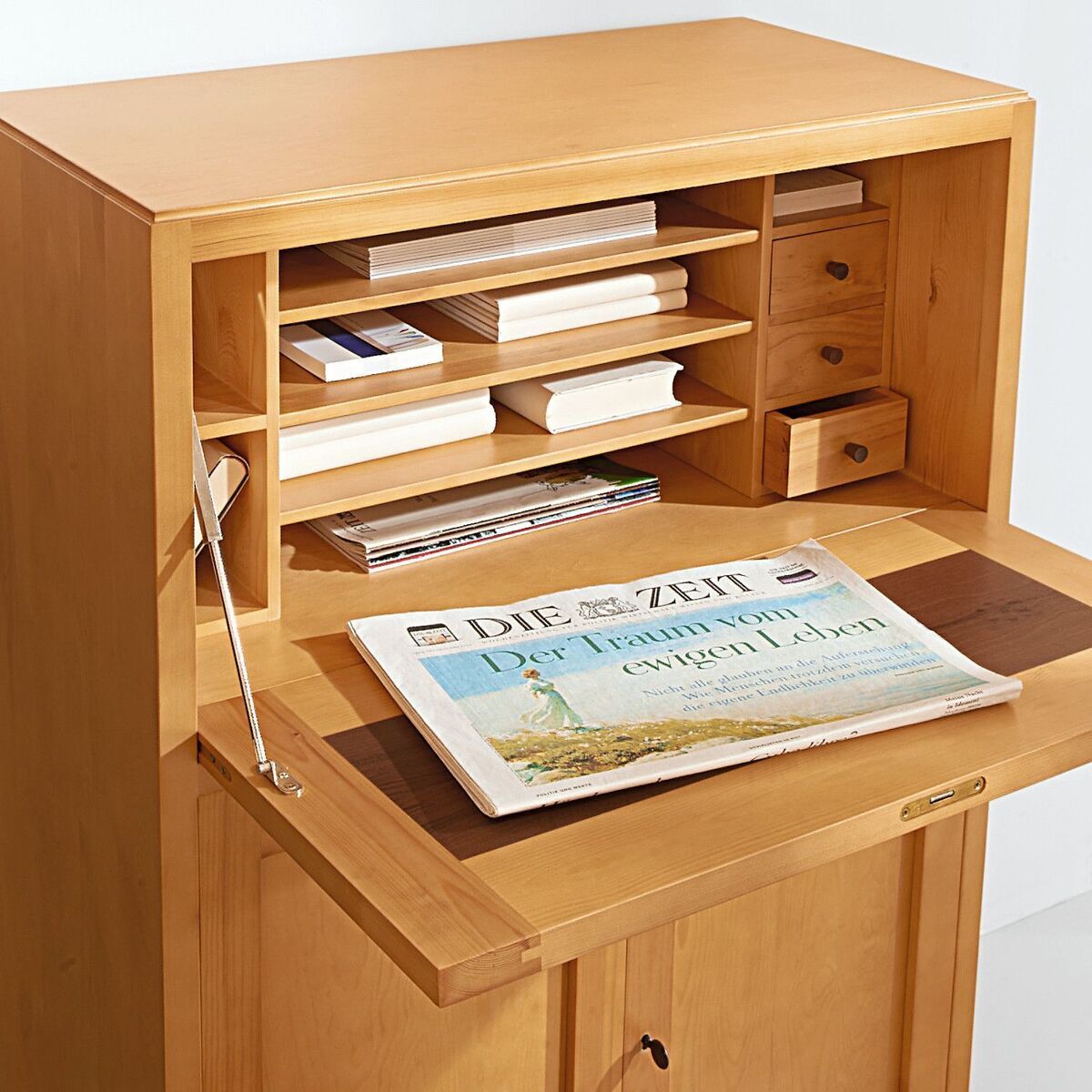 Ein hölzerner Schreibtisch der Marke MARKTEX in der Sonderedition ZEIT-Sekretär. Der Schreibtisch verfügt über offene Einlegefächer, Schubladen und eine Zeitung. Die Oberfläche ist in einem natürlichen Holzbraun gehalten.