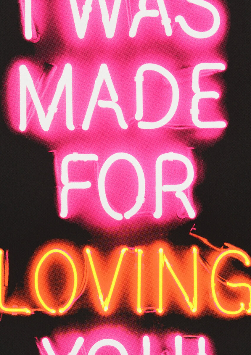 Neon-Kunstwerk mit der Aufschrift 'I WAS MADE FOR LOVING YOU' in leuchtendem Pink und Orange auf schwarzem Hintergrund.