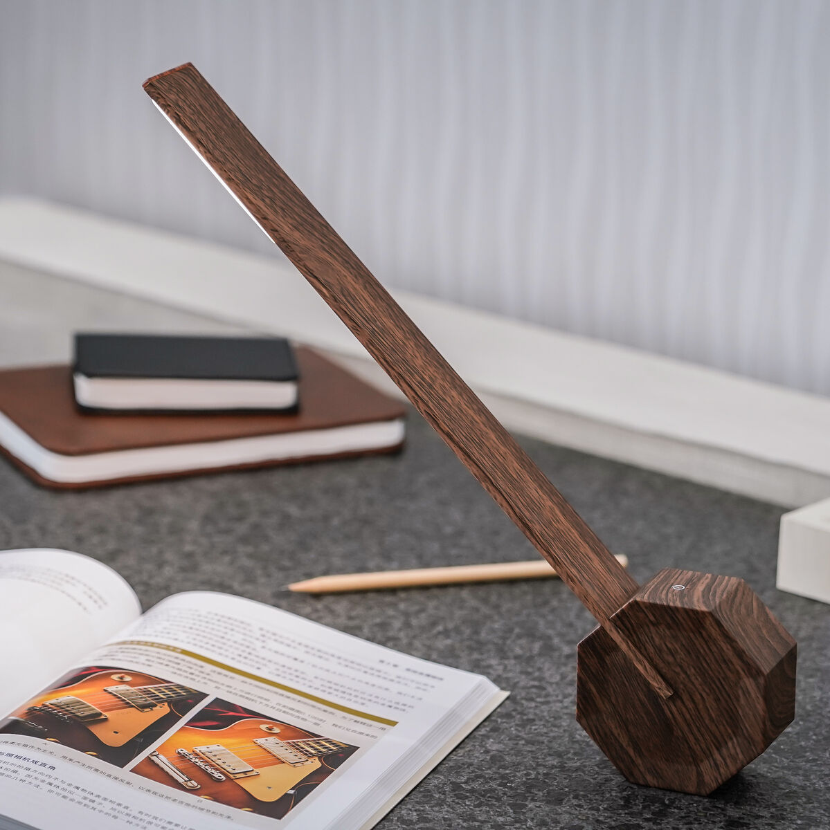 Eine moderne Tischlampe aus Holz in achteckiger Form steht auf einem grauen Tisch. Im Hintergrund sind Bücher, ein Bleistift und eine digitale Uhr zu sehen. Das Umfeld strahlt Eleganz und Minimalismus aus, perfekt für ein Arbeitszimmer oder Wohnzimmer.