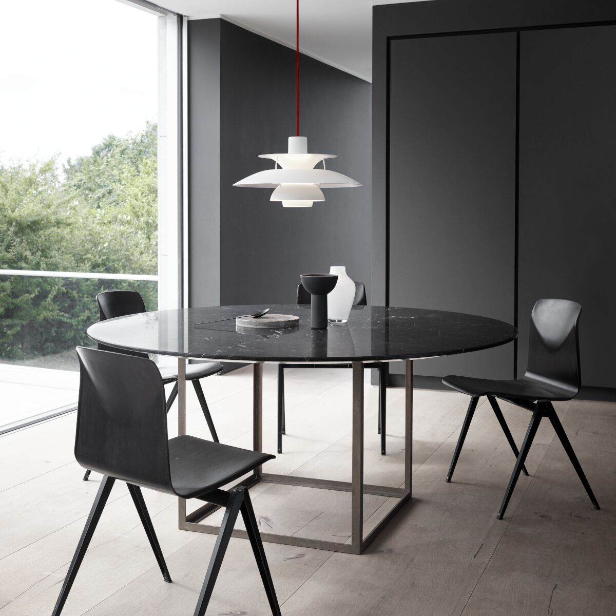 Ein rundes, modernes Esszimmer mit einer weißen und roten PH5 Monochrome Pendelleuchte als Blickfang über einem schwarzen Tisch. Die Szene zeigt stilvolle schwarze Stühle, große Fenster mit Blick ins Grüne und eine minimalistische, elegante Raumgestaltung.