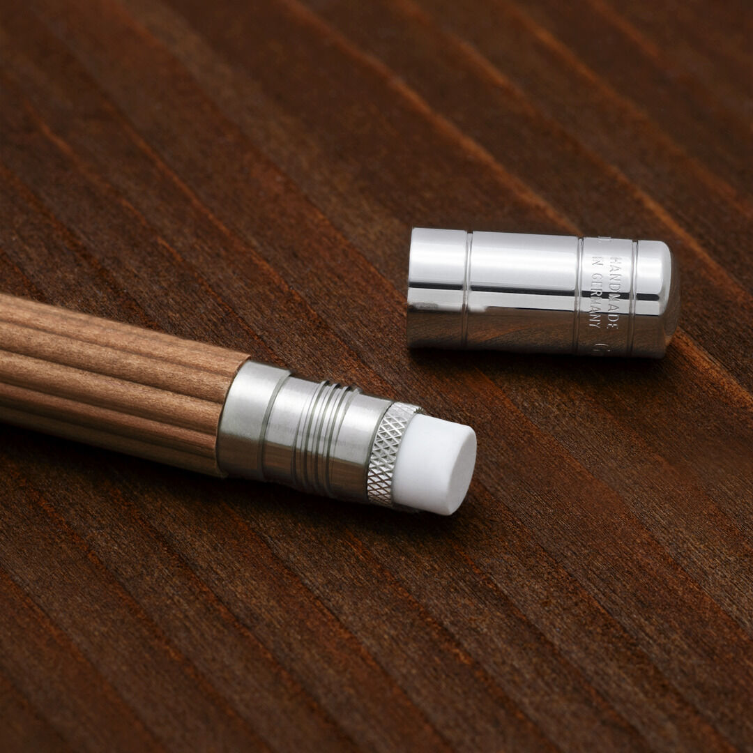Ein Perfekter Bleistift aus Holz mit einer glänzenden silbernen Metallkappe und einem weißen Radiergummi liegt auf einer dunklen Holzoberfläche. Die Kappe ist abgenommen und liegt separat daneben.