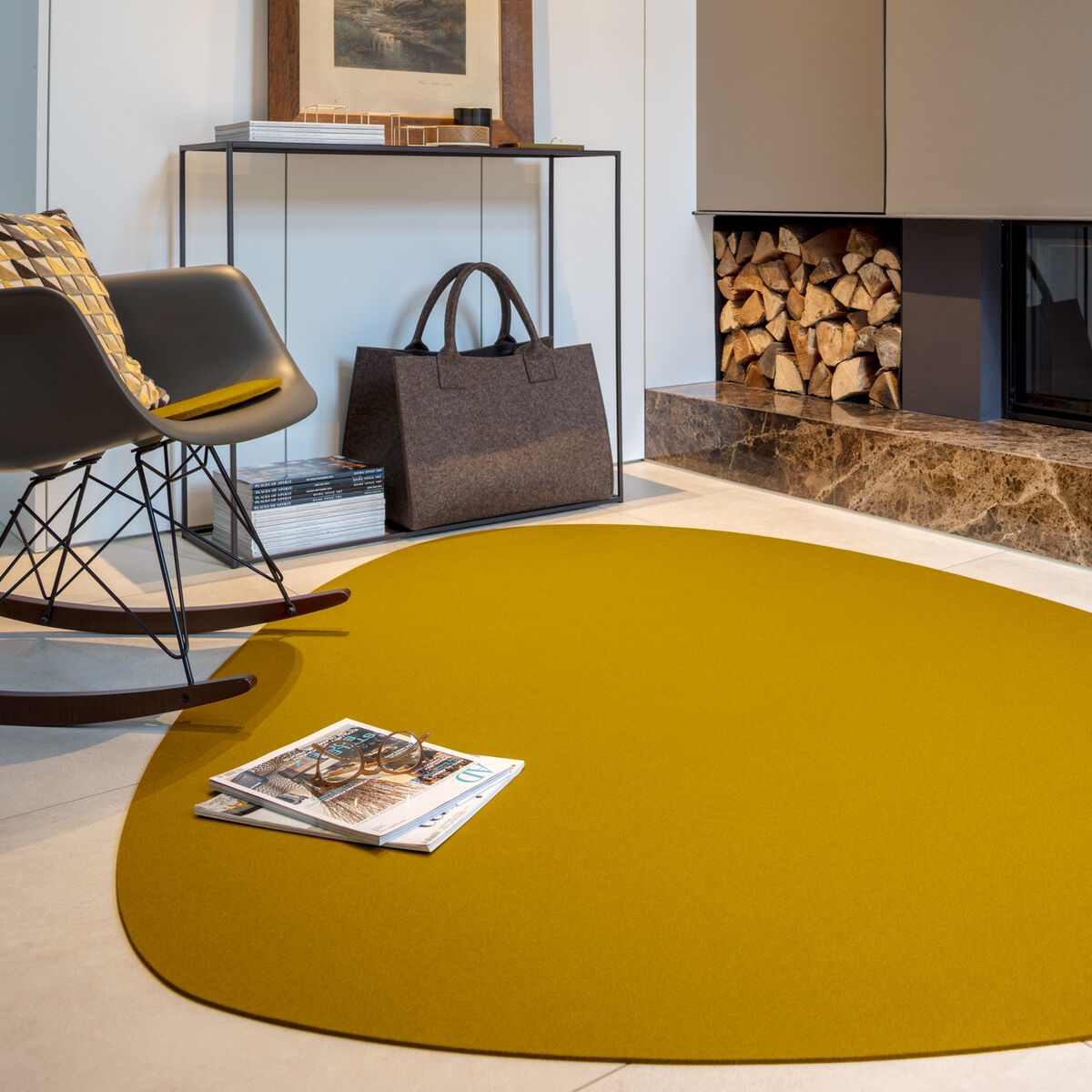 Ein modernes Wohnzimmer mit einem gelben Teppich »Stone«, einer schwarzen Stuhl, einem niedrigen Tisch und einem Kamin im Hintergrund. Der Teppich hat eine unregelmäßige Form und passt gut zu den neutralen Farben des Raums.