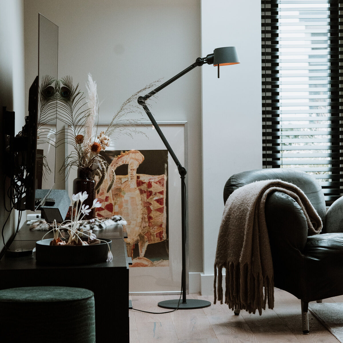 Eine moderne Stehlampe mit zwei Armen, Modell »BOLD (2arm)«, steht in einem geschmackvoll eingerichteten Wohnzimmer neben einem Sessel und trägt zur gemütlichen Atmosphäre bei.