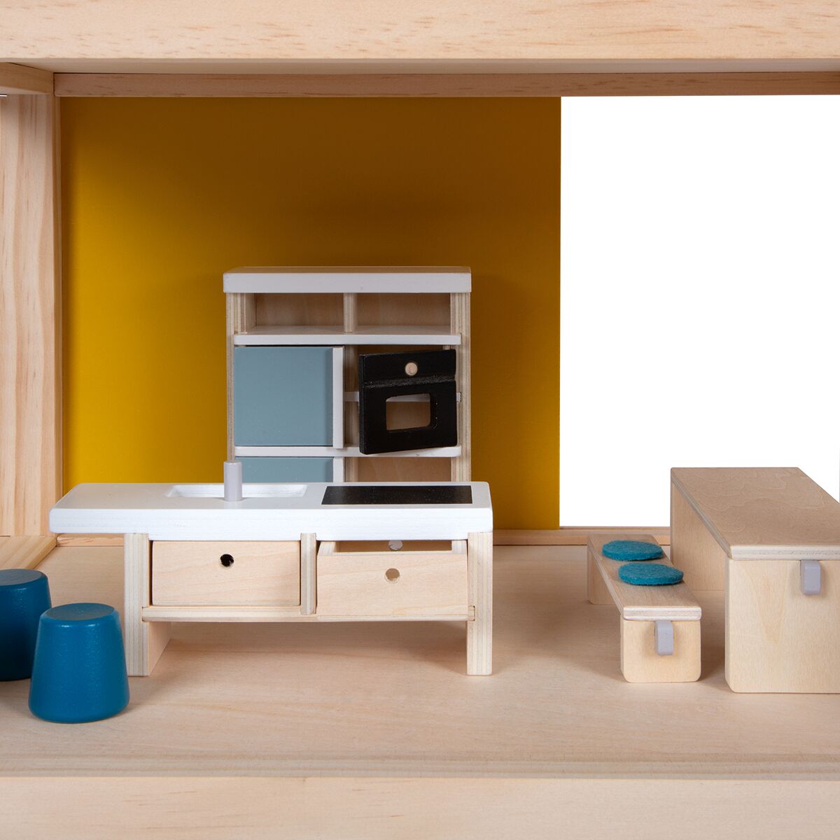 Detailansicht eines Puppenhauses aus Holz mit modernen Miniaturmöbeln; im Vordergrund ein Küchenblock mit weißen und schwarzen Elementen, Schränken und Hockern auf einem naturfarbenen Holzboden, gelb abgesetzte Rückwand.