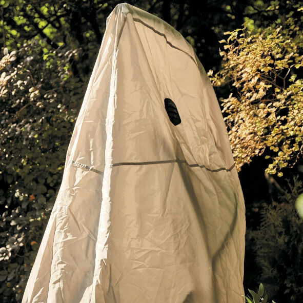 Die Schutzhülle »Aquashield« von Sienagarden aus beigem Polyester bedeckt ein großes Möbelstück im Garten. Die wetterfeste, wasserabweisende Hülle wirkt hochwertig, besitzt eine Lüftungsöffnung und steht zwischen grünen und gelblichen Pflanzen.