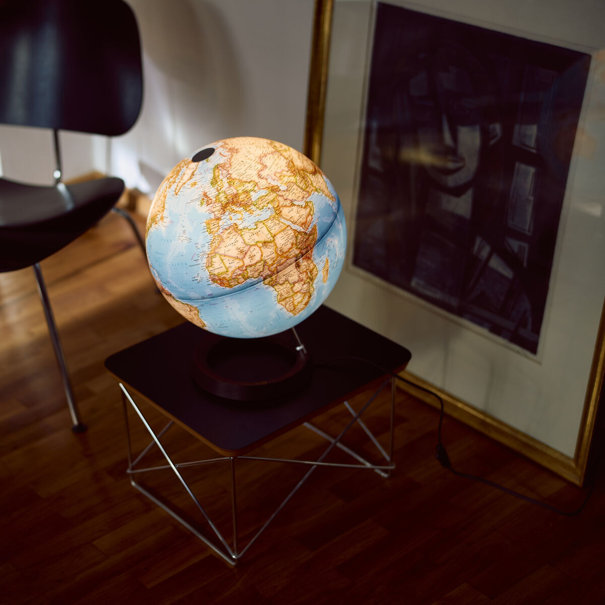 Ein klassischer Globus von National Geographic auf einem Tisch im Wohnzimmer, umgeben von einem Stuhl und einem gerahmten Bild. Der Globus zeigt eine detaillierte Weltkarte in Blau und Orange.