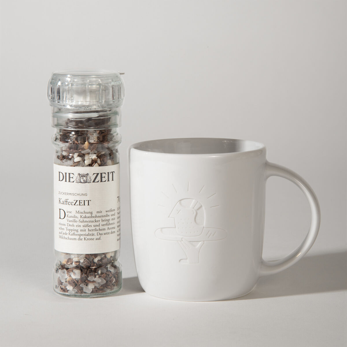 Ein Geschenkset bestehend aus einer weißen Tasse mit einem geprägten Vogelmotiv und einer Gewürzmischung von 'Die Zeit' mit dem Etikett 'KaffeeZEIT'.
