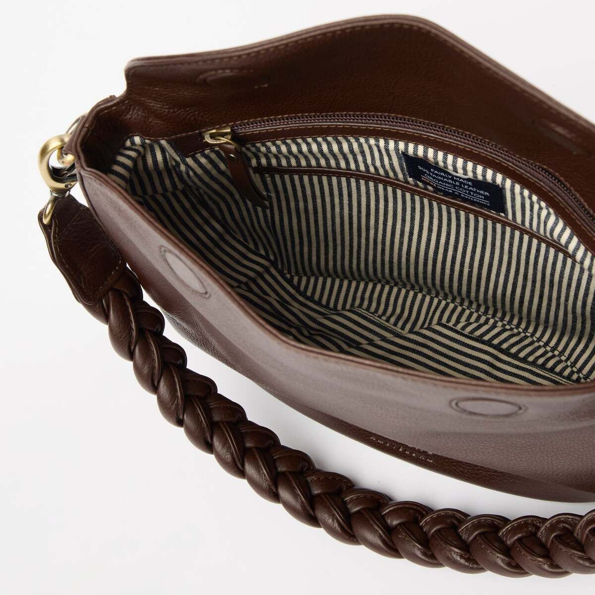 Braune Ledertasche mit geflochtenem Henkel, geöffnet und mit einem gestreiften Innenfutter sowie einem Reißverschlussfach, fotografiert auf hellem Hintergrund. Modeaccessoire für Frauen, geeignet für Alltag und besondere Anlässe.