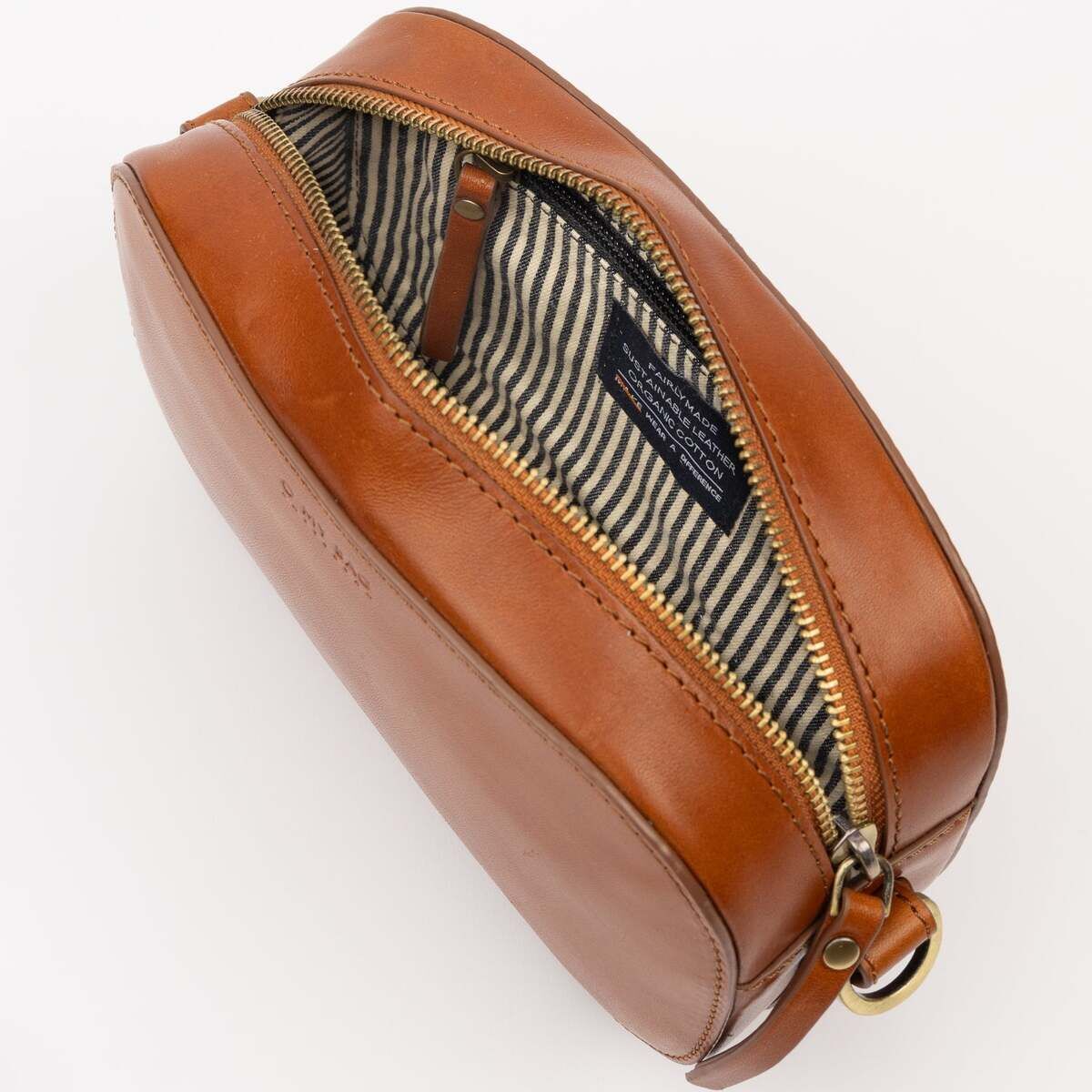 Abgebildet ist eine kleine Umhängetasche namens »Maya« aus braunem Leder mit goldenem Reißverschluss. Das Innere der Tasche ist mit einem gestreiften Stoff ausgekleidet. Die Tasche steht vor hellem Hintergrund und ist leicht geöffnet, sodass das Innenfutter sichtbar wird.