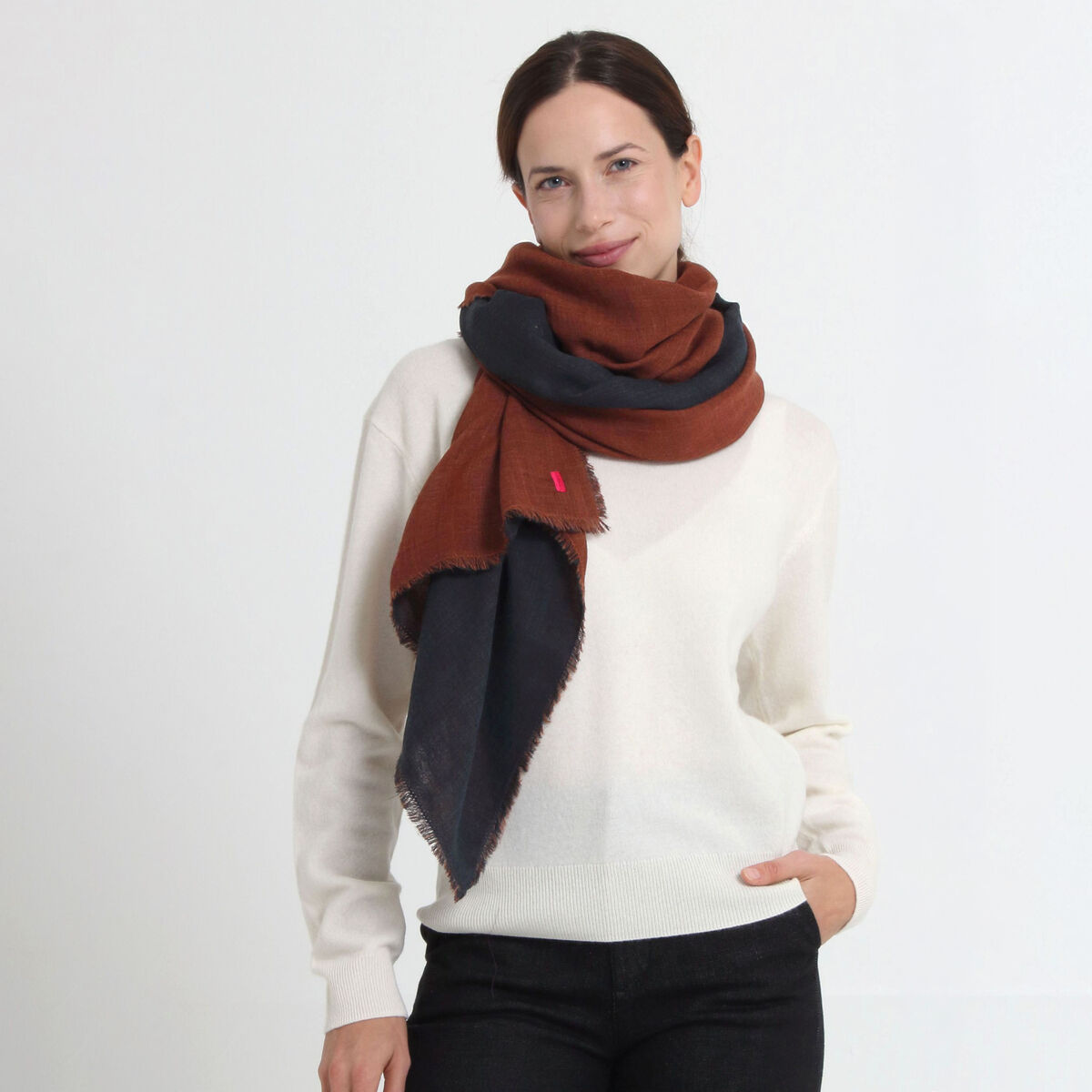 Eine Frau trägt den zweilagigen Wollschal »Carla« von Shalls Barcelona in Anthrazit-Kupfer locker um den Hals über einem weißen Pullover. Der Schal wirkt weich, voluminös und stilvoll; ideal für Herbst und Winter, 200 x 70 cm groß.