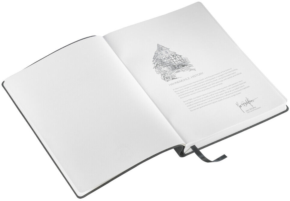 Ein geöffnetes Notizbuch im DIN A5-Format mit einem weißen Umschlag und Blankoseiten. Das erste Blatt enthält eine Illustration und einen Text auf Englisch. Ein schwarzes Lesezeichen ist angebracht.