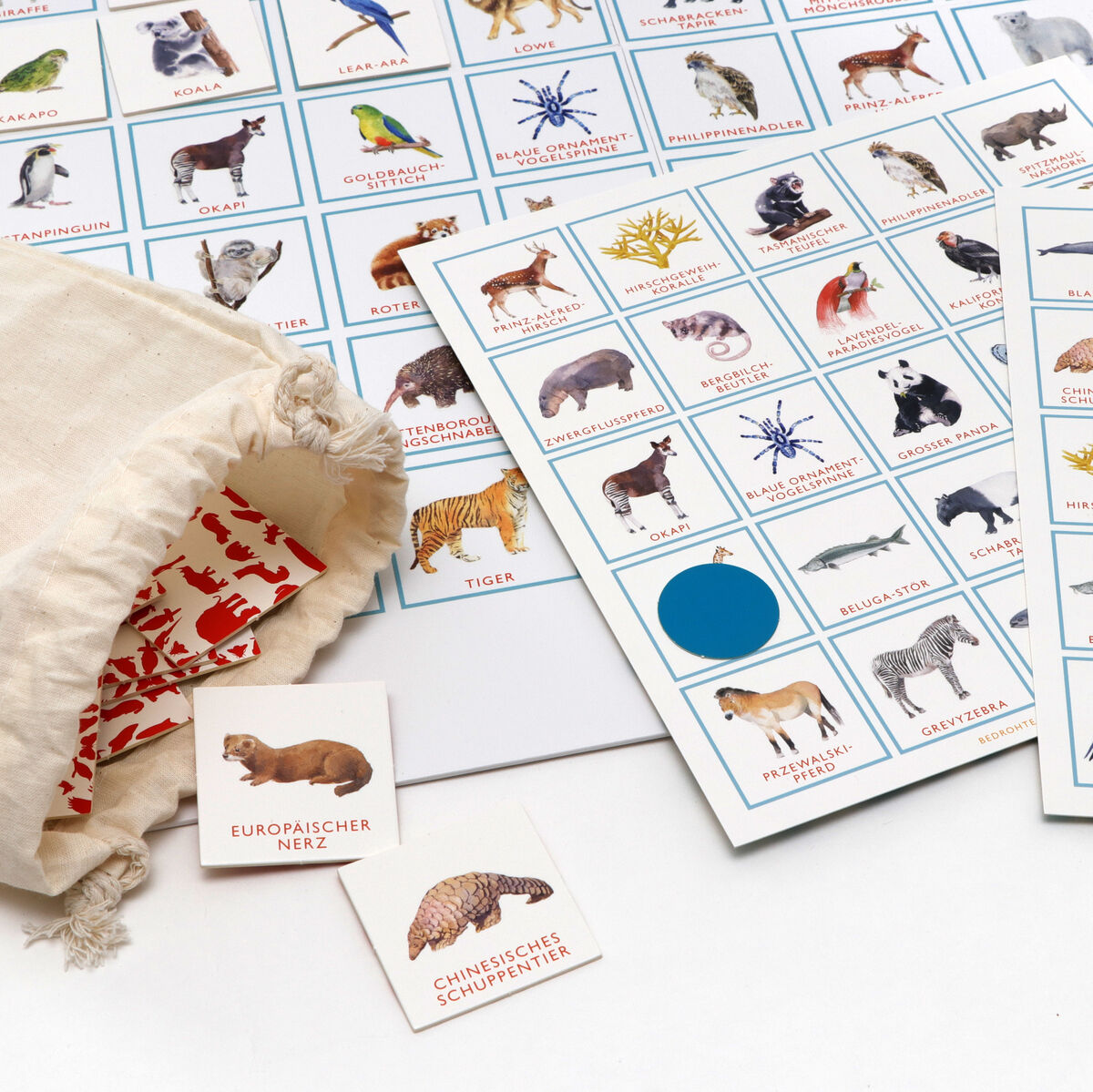 Bingo-Spiel »Bedrohte Tiere« mit mehreren Tierkarten, einem Spielplan und einem Beutel mit roten Tiermotiven auf weißem Hintergrund.