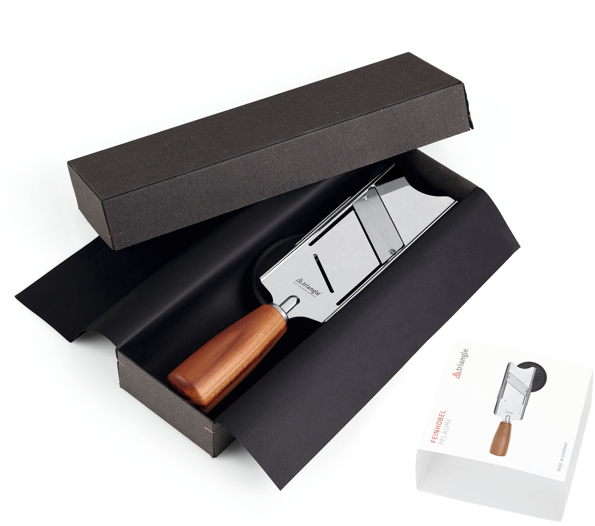 Feinhobel aus Edelstahl und Pflaumenholz in einer schwarzen Geschenkbox, daneben eine weiße Verpackung.