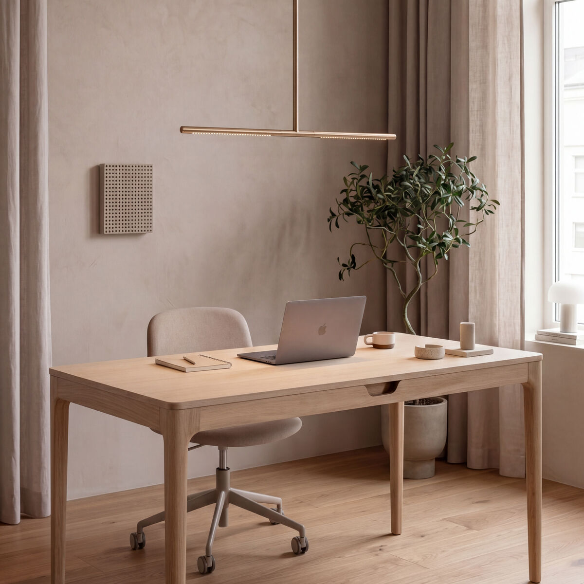Heller, minimalistischer Arbeitsbereich mit dem Schreibtisch »Heart'n'Soul« von Umage aus hellem Holz, darauf Laptop, Notizbuch, Becher und Stifte. Dezente Deko mit kleiner Pflanze, moderne Messing-Deckenleuchte, helle Vorhänge und viel Tageslicht durch großes Fenster.