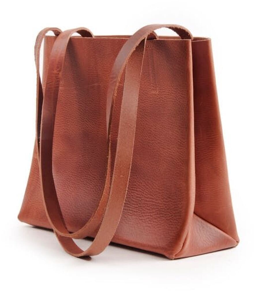 Eine elegante braune Ledertasche im Papierbeutel-Stil mit zwei langen Riemen, steht aufrecht gegen einen weißen Hintergrund, minimalistisch und modern.