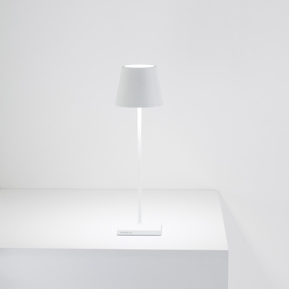 Bild einer modernen, minimalistisch gestalteten LED-Tischlampe namens »Poldina Pro« in Weiß und Grau. Die Lampe steht auf einer weißen Oberfläche und hat ein schlichtes, elegantes Design.