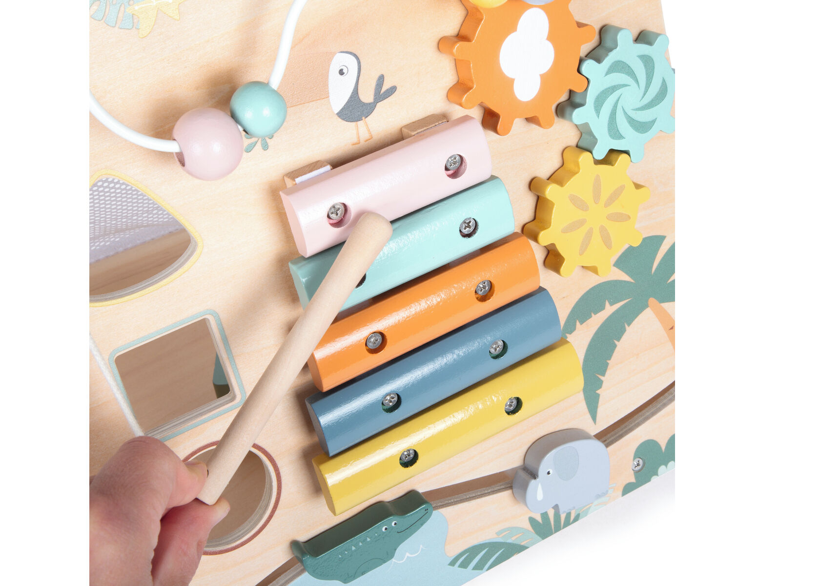 Nahaufnahme eines bunten Lauflernwagens aus Holz mit Safari-Motiv. Zu sehen sind ein Xylophon mit fünf pastellfarbenen Klangstäben und mehrere Zahnräder in Gelb, Orange und Grün. Eine Kinderhand hält einen Holzstab und spielt auf dem Xylophon. An der Seite sind Illustrationen von Tieren und Palmen erkennbar.