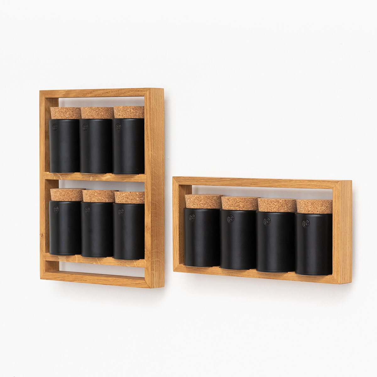 Das Bild zeigt zwei moderne Gewürzregale aus Holz, beide bestückt mit schwarzen Gewürzbehältern und Korkverschlüssen. Ein Regal ist vertikal und das andere horizontal montiert. Die weiße Hintergrundwand betont das minimalistische Design.