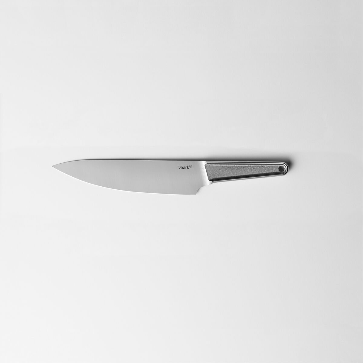 Ein Küchenmesser aus rostfreiem Stahl mit einem silbernen, ergonomisch geformten Griff. Das Messer liegt flach auf einer weißen Oberfläche.