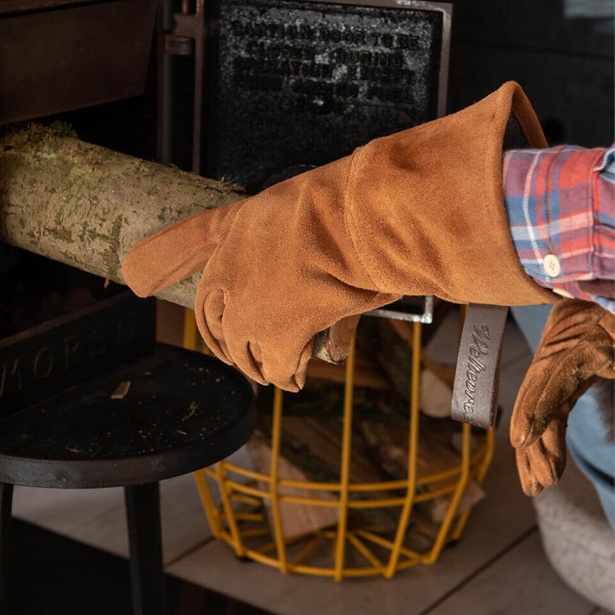 Eine Person trägt Handschuhe aus Rindleder und bewegt ein Stück Holz in einen Kamin. Der Handschuh ist braun und robust, ideal für körperliche Arbeiten im Freien oder zum Tragen von Holz.