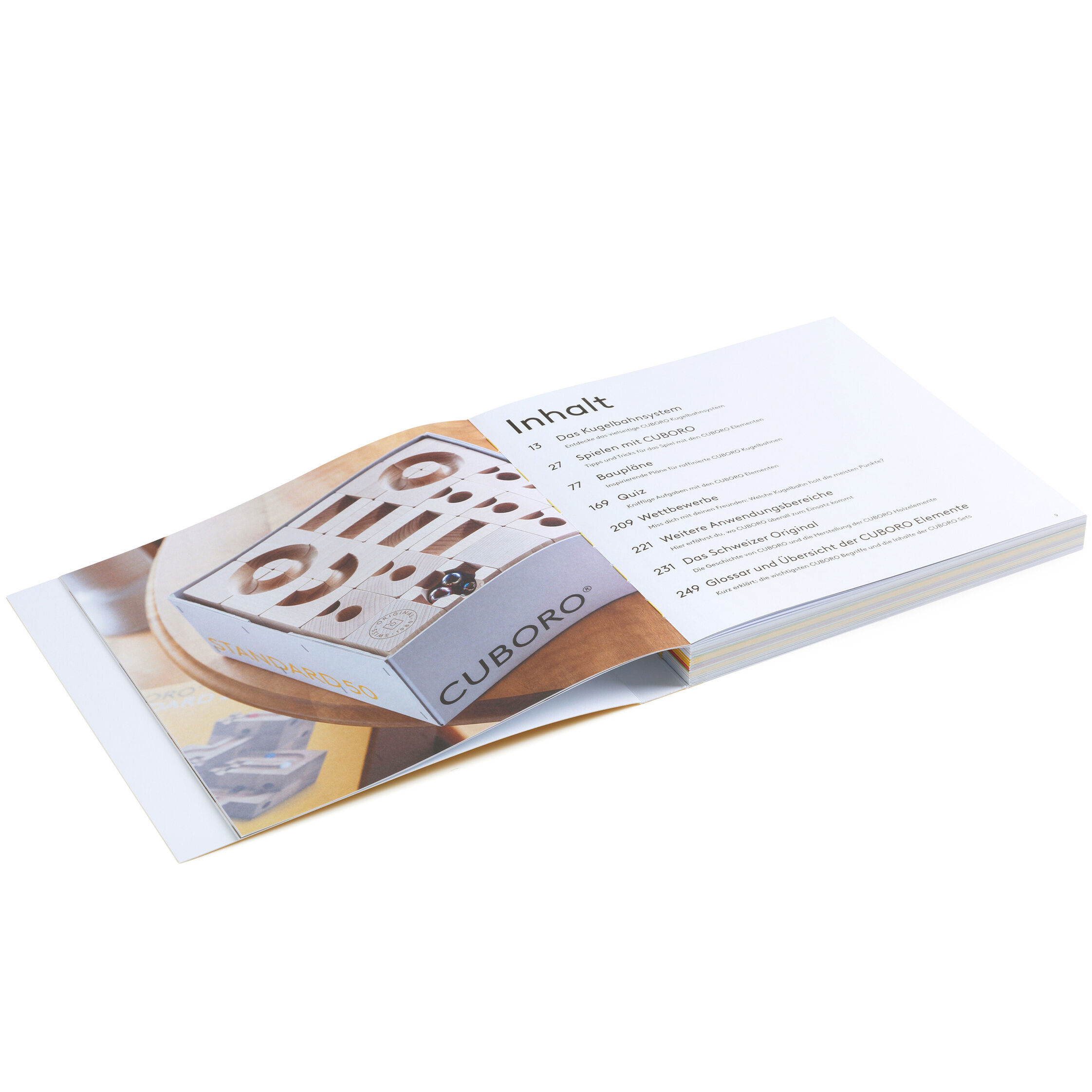 Das Bild zeigt das aufgeschlagene Buch „CUBORO – DAS BUCH“. Sichtbar ist ein Inhaltsverzeichnis sowie eine großformatige Fotografie eines Cuboro Kugelbahnsets auf der linken Buchseite. Das Design ist modern und klar, Farben sind überwiegend weiß, beige und zarte Holztöne.