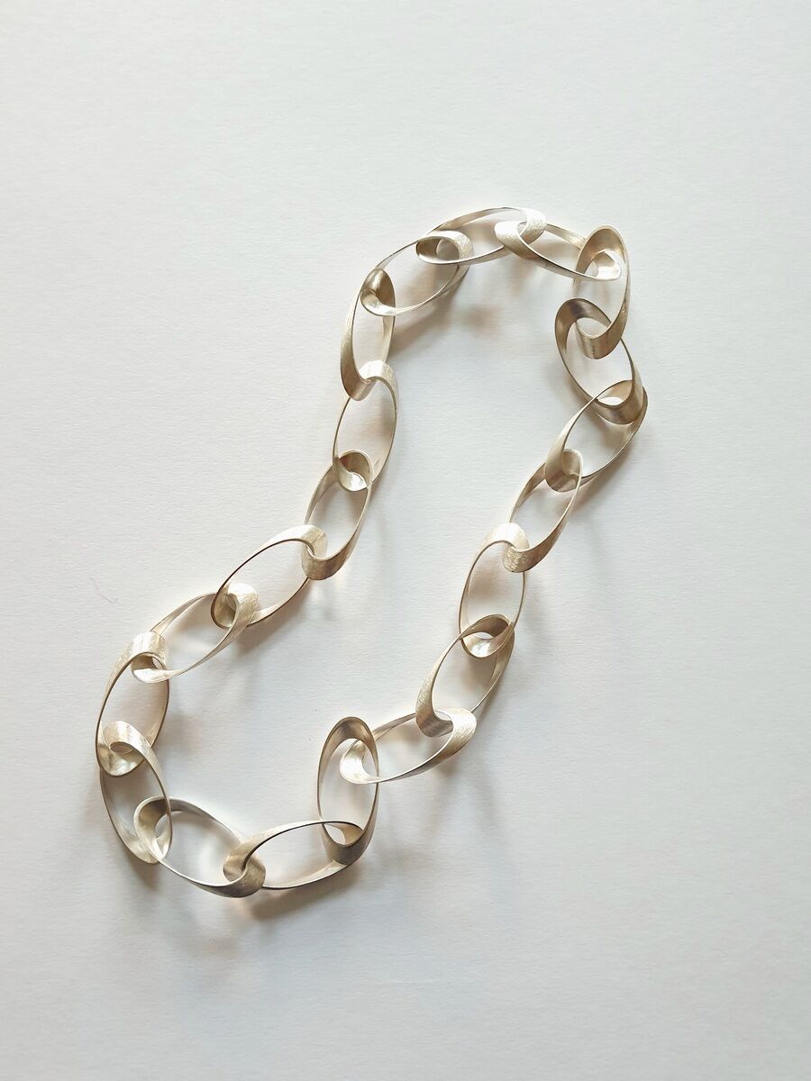 Eine elegante Halskette mit großen, ovalen Gliedern in Gold, die auf einem weißen Hintergrund liegt. Das Design wirkt modern und minimalistisch.