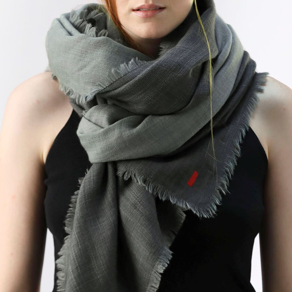 Grauer Wollschal im Doubleface-Design, locker um den Hals einer Frau gelegt. Das schlichte Accessoire ist aus weichem, hochwertigem Material gefertigt und hat eine dezente Fransen-Kante. Eleganter Schal für Herbst und Winter.
