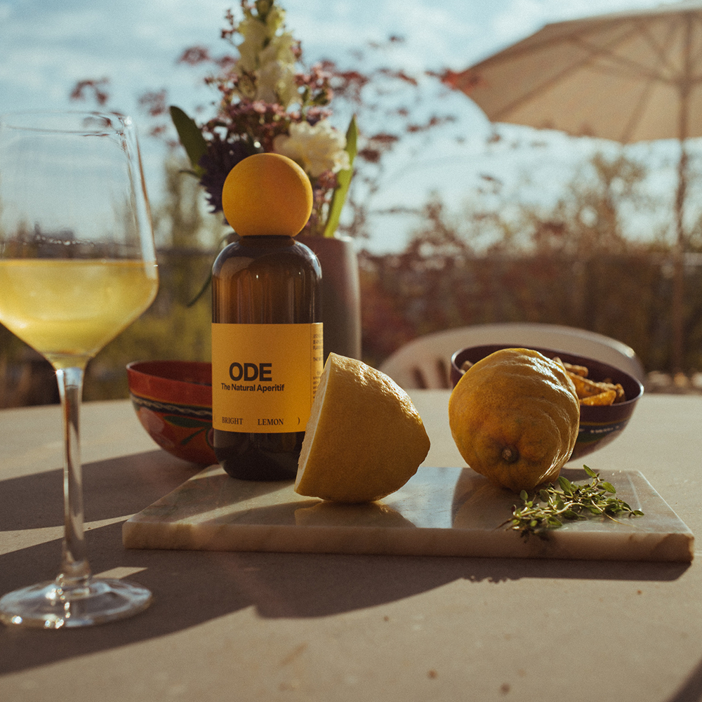 Braune Flasche mit gelbem Etikett 'ODE The Negroni Aperitif', Zitronen, Thymianzweig und Glas mit gelbem Getränk auf Tisch im Freien