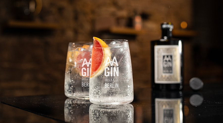 Zwei Gläser mit Gin Tonic, eines mit Grapefruitscheibe, im Hintergrund Flasche mit Aufschrift 'AA GIN BERLIN'