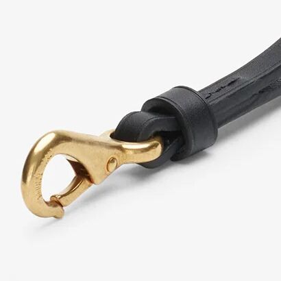 Nahaufnahme eines eleganten Schlüsselanhängers aus schwarz gefärbtem, pflanzlich gegerbtem Rindleder mit goldfarbenem, massivem Karabinerhaken aus Messing. Das Lederband ist sauber verarbeitet und zeigt feine Prägelinien sowie polierte Kanten.