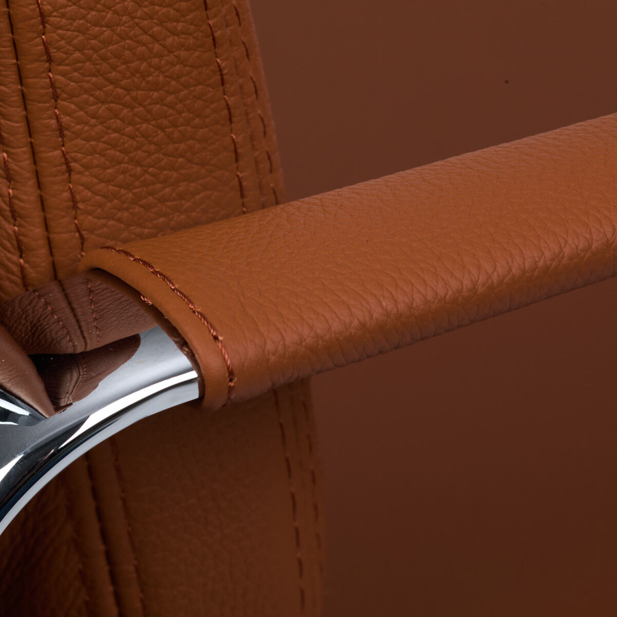 Detailaufnahme vom Vitra Soft Pad EA219 Schreibtischstuhl der ZEIT-Sonderedition: Nahansicht zeigt die gepolsterte, mit cognacfarbenem Leder bezogene Armlehne und das glänzend verchromte Metallgestell. Hochwertige Verarbeitung und feine Steppnähte sind sichtbar.