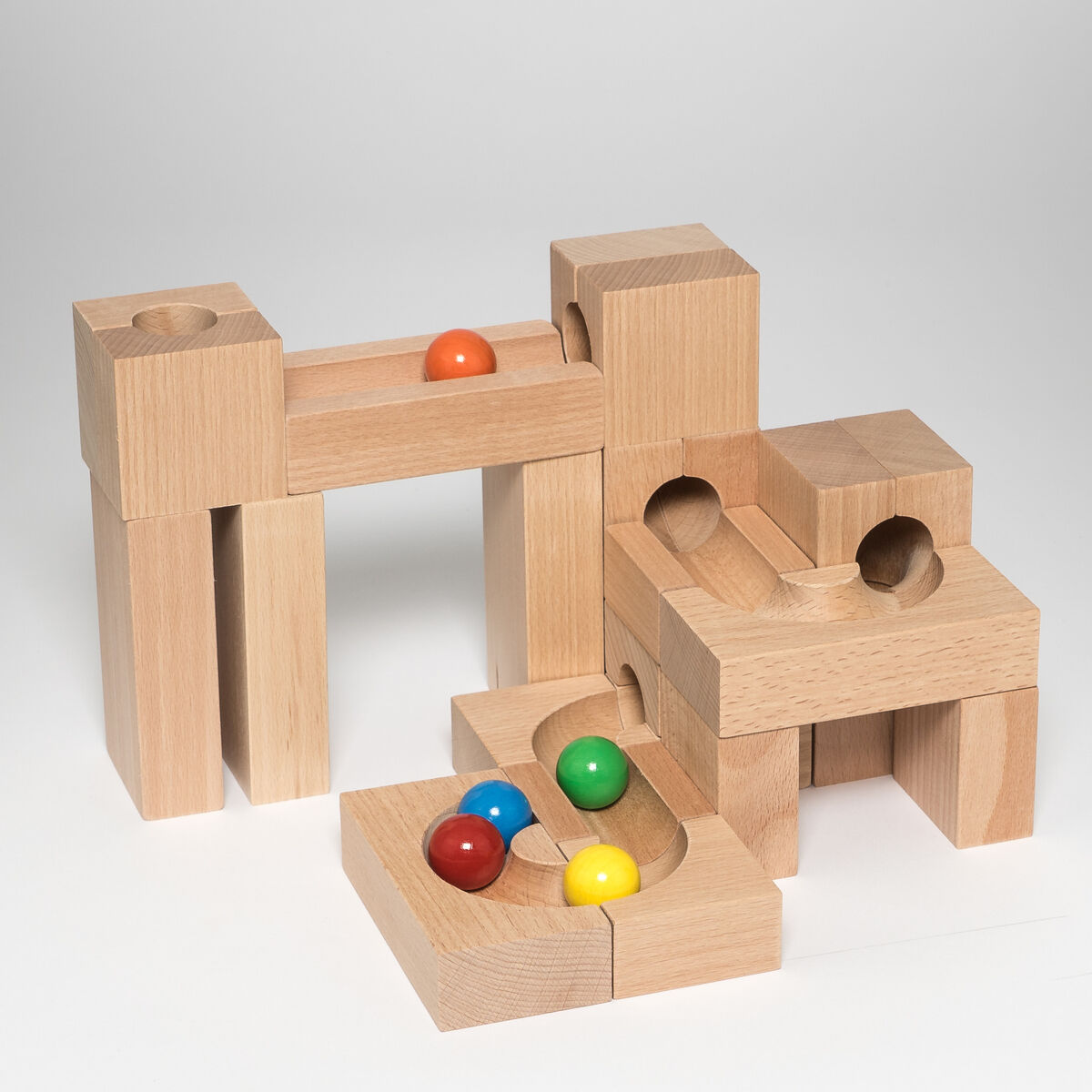 Eine Kugelbahn aus Holz bestehend aus verschiedenen naturbelassenen Holzklötzen, die zusammengebaut sind. Auf den Holzklötzen befinden sich bunte Holzkugeln in den Farben Gelb, Rot, Grün und Blau.
