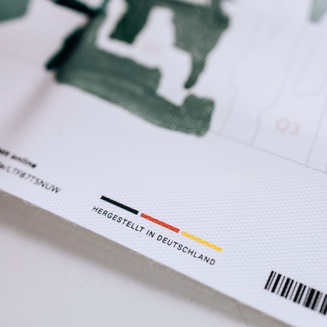 Ein Nahaufnahme eines „Malen nach Zahlen“-Kits mit einigen grünen Abschnitten, einem Barcode und einem Hinweis zur Herstellung in Deutschland. Die Farben Grün, Weiß, Schwarz, Rot und Gelb sind sichtbar.