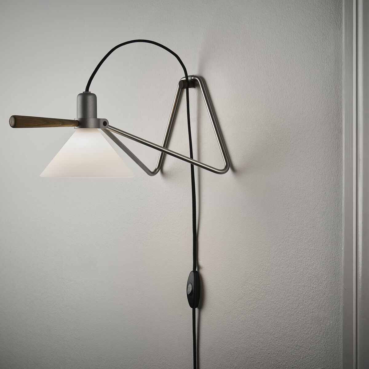 Bild einer Tisch-/Hängelampe namens »Spot« mit modernem, industriellem Design. Die Lampe hat einen schwenkbaren Arm und eine Metallfassung, die an einer Wand montiert ist. Die Beleuchtung ist direkt und fokussiert, ideal für Innenräume.