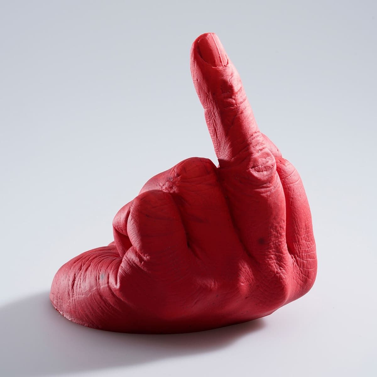 Eine rote Skulptur einer Hand, die von Ai Weiwei entworfen wurde. Die Hand zeigt den Mittelfinger in einer Perspektive, die die Bedeutung der Perspektive im Kunstwerk betont. Der Hintergrund ist weiß.