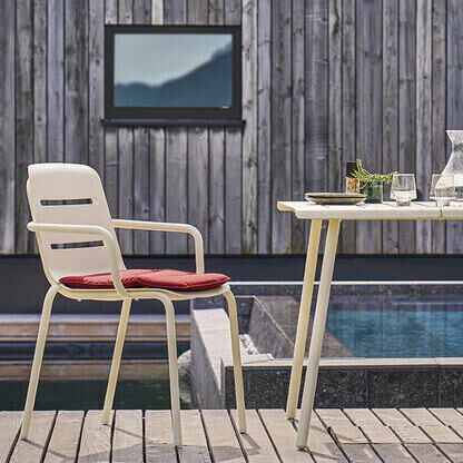 Zwei bequeme Sessel »VAPIO« und ein runder Tisch auf einer Holzterrasse am Pool vor einem modernen Gebäude.