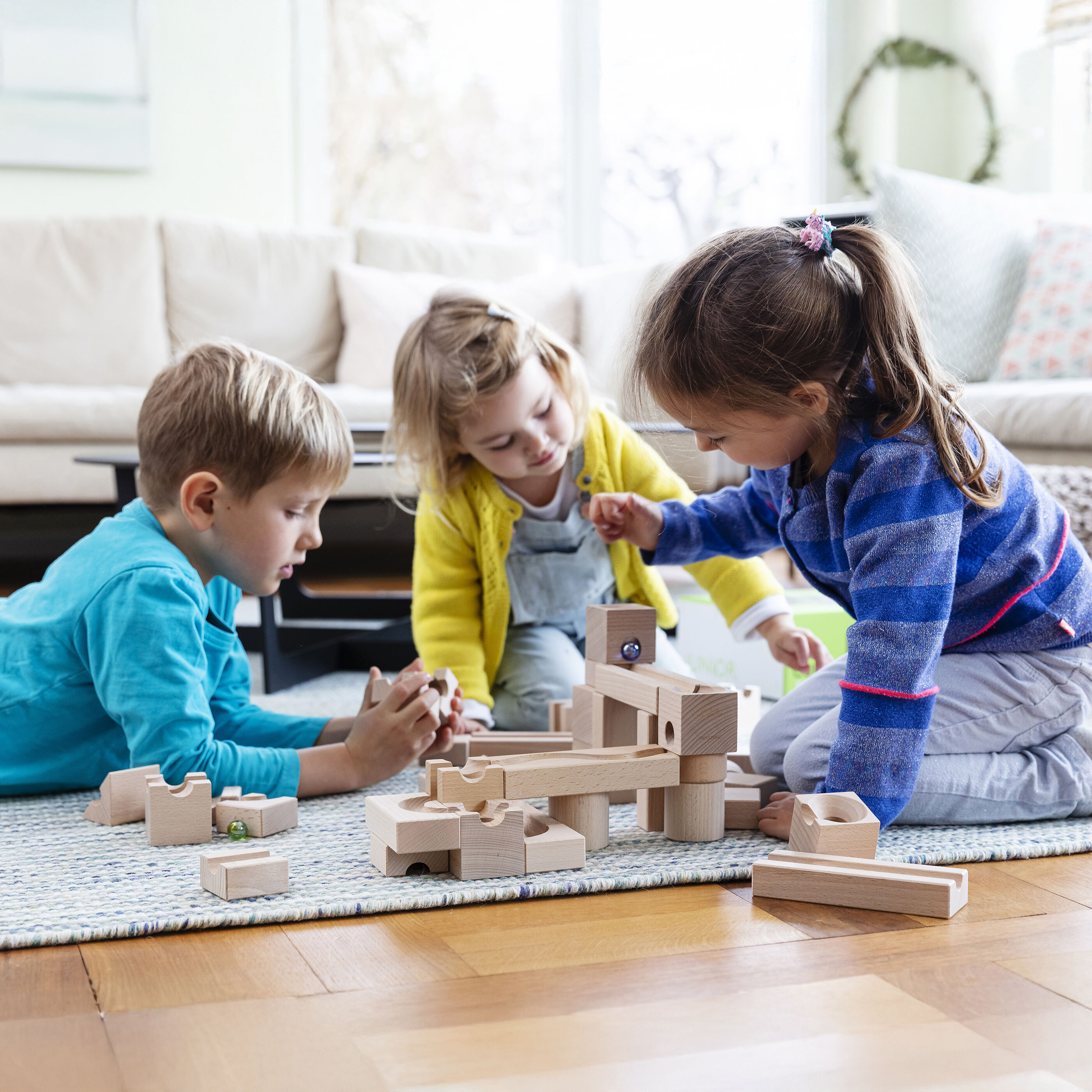 Die Kugelbahn Starter-Set »JUNIOR« von Cuboro ist aus naturbelassenem hellem Schweizer Holz gefertigt und besteht aus 40 Würfel- und Schienenelementen sowie bunten Kugeln. Die Bauteile liegen sortiert auf hellem Untergrund, die Szene wirkt freundlich, hochwertig und pädagogisch ansprechend.