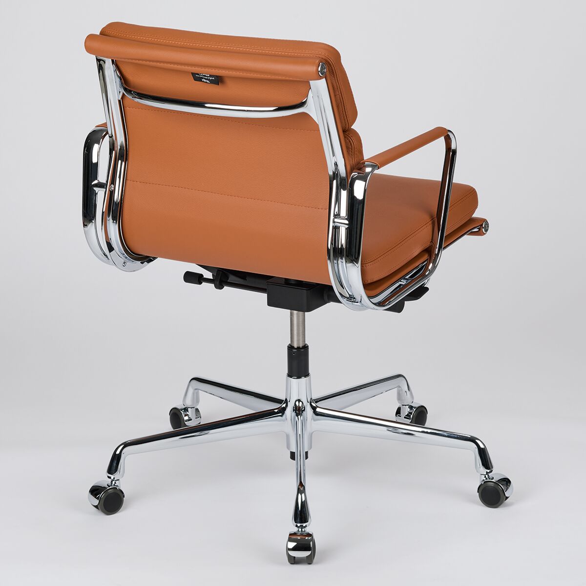 Rückansicht eines Vitra Soft Pad EA217 Bürostuhls mit braunem Lederbezug und chromfarbenem Gestell auf Teppichrollen.