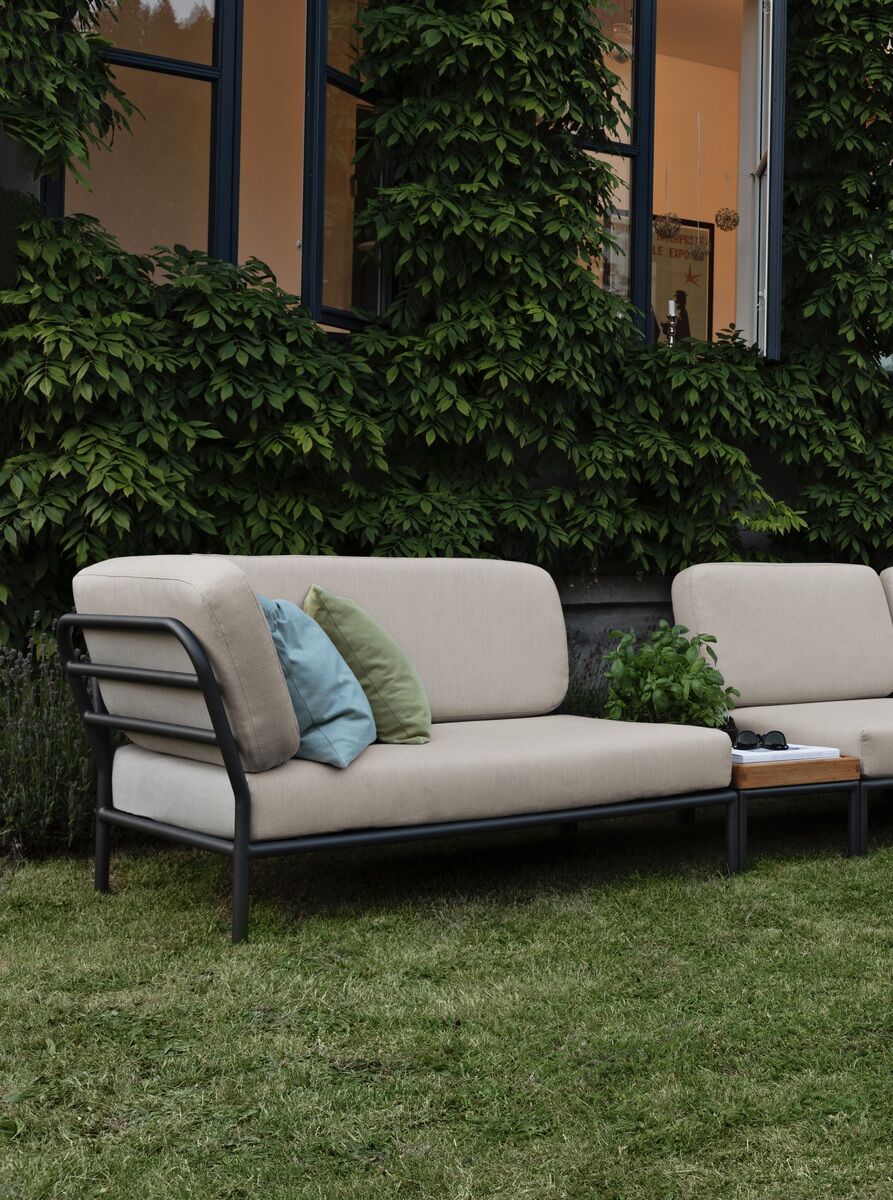 Lounge-Ecke der Modellreihe »LEVEL« mit einem linken Modul, bestehend aus einem bequemen, weißen Polster und einem robusten Metallrahmen. Das Sofa steht auf grünem Rasen vor einer mit Efeu bewachsenen Fassade. Im Hintergrund sind offene Fenster zu sehen.